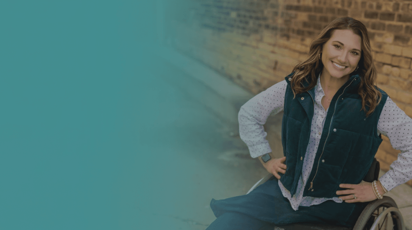 Kristen smiling confidently in her wheelchair against a brick wall