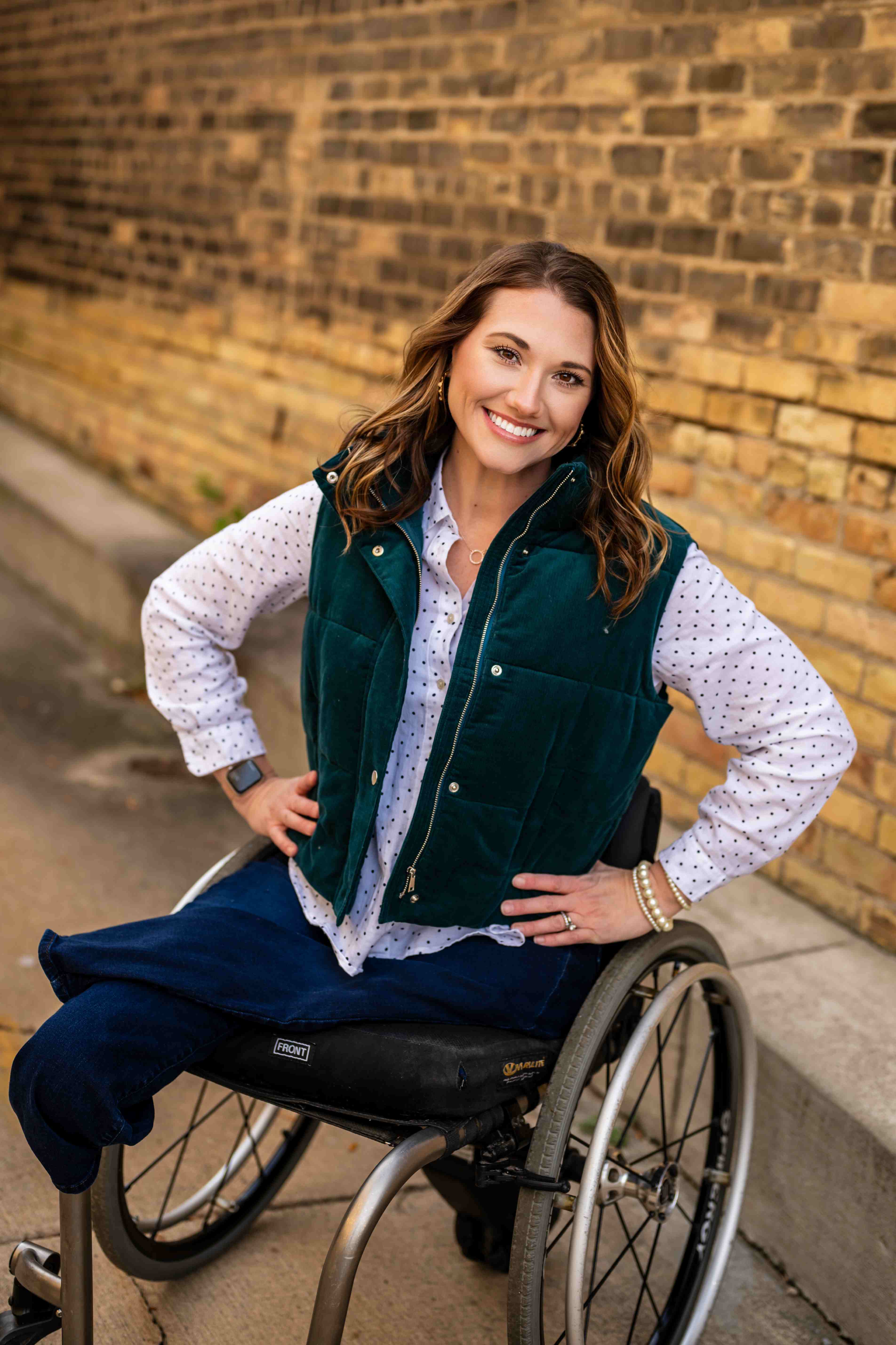 Kristen smiling confidently in her wheelchair wearing a green vest
